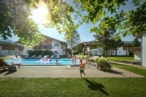 Outdoor Pool Lisi Family Hotel Personen in einem Außenpool vor Hotelgebäuden bei Sonnenschein.