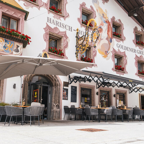 Das charmante Restaurant Goldener Greif in Kitzbühel zeigt eine malerische Fassade mit bunten Blumen und kunstvollen Wandmalereien.