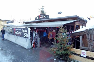 Außenansicht des Hahnenkamm Pavillons mit Skifahrern und abgestellten Skiern unter einer Markise.