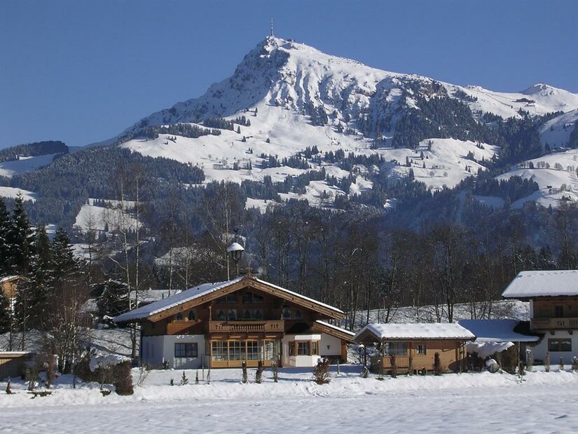 Eine malerische Winterlandschaft mit schneebedeckten Bergen im Hintergrund. Im Vordergrund sind charmante, traditionelle Holzhäuser zu sehen.