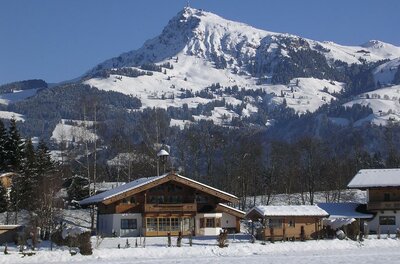 Ferienwohnung Gandler 01 Eine malerische Winterlandschaft mit schneebedeckten Bergen im Hintergrund. Im Vordergrund sind charmante, traditionelle Holzhäuser zu sehen.