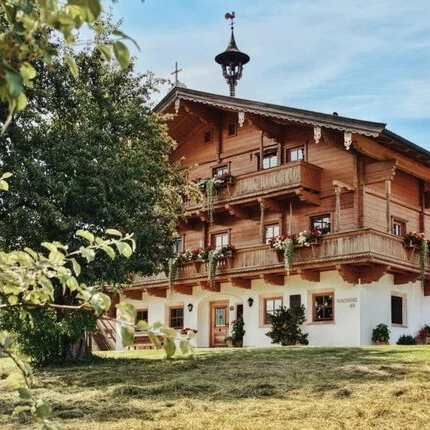 Ein traditionelles Holzhaus mit mehreren Balkonen, umgeben von üppigem Grün und blühenden Pflanzen im Vordergrund.