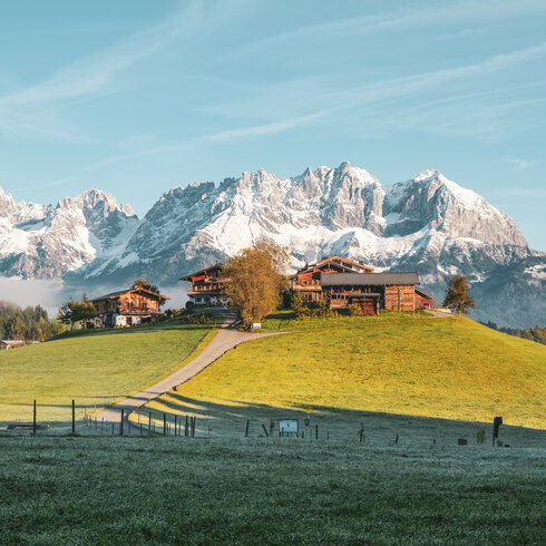 Eine malerische Landschaft mit schneebedeckten Bergen und traditionellen Holzhäusern auf einer sanften Hügelkuppe.