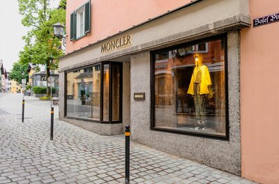 Außenansicht eines Moncler-Geschäfts in einer gepflasterten Fußgängerzone mit Schaufensterpuppe.