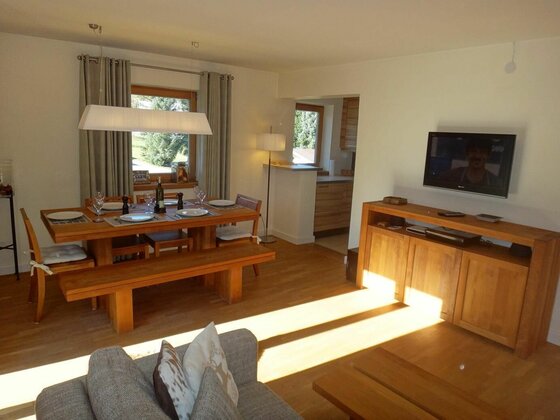 Moderner Essbereich aus Holz mit gedecktem Tisch, Sitzbank und angrenzendem Wohnzimmer mit TV.