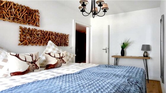 Modernes Schlafzimmer mit Doppelbett, Kissen mit Hirschmotiven und Wanddekoration aus Holzästen.