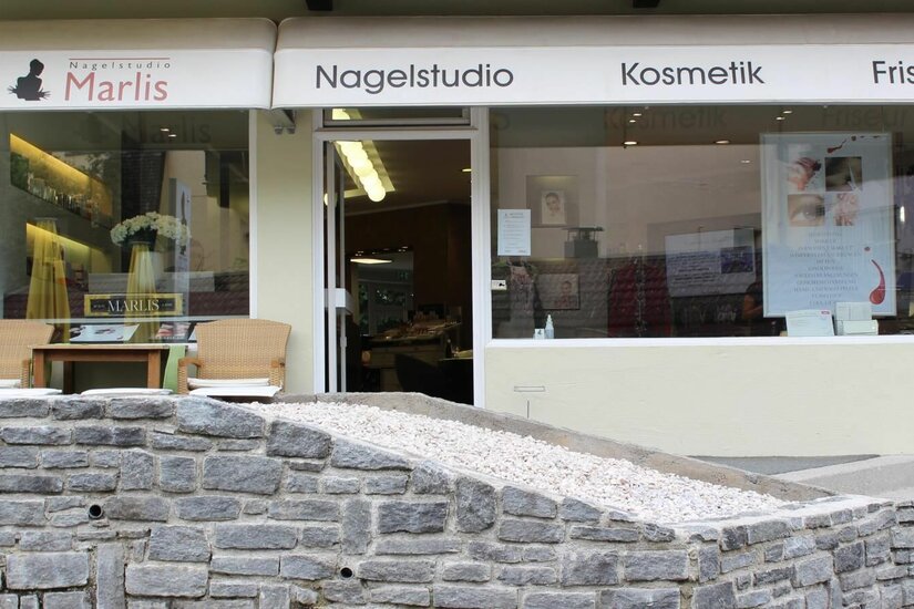 Außenansicht des Beauty Centers Marlis mit Schaufenstern, Markise und einer Natursteinmauer im Vordergrund.