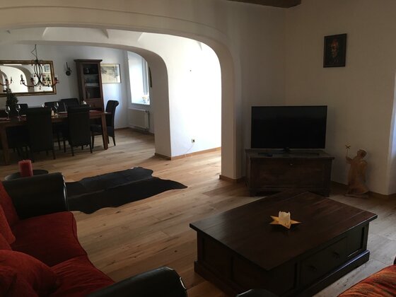 Wohnbereich im Appartement Wohnzimmer mit rotem Sofa, dunklem Holztisch und Fernseher, im Hintergrund ein Essbereich mit Holzboden.