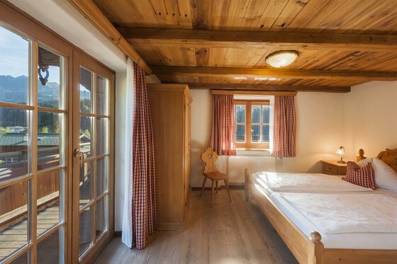 Rustikales Doppelzimmer mit Holzdecke, Doppelbett, Schrank und Balkonzugang.
