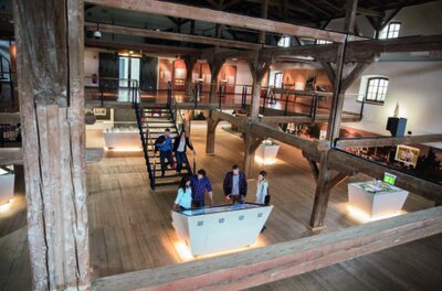 Ausstellung in der Stiegl-Brauwelt Innenansicht einer Ausstellung in einem historischen Holzgebäude mit Besuchern und Informationstafeln.