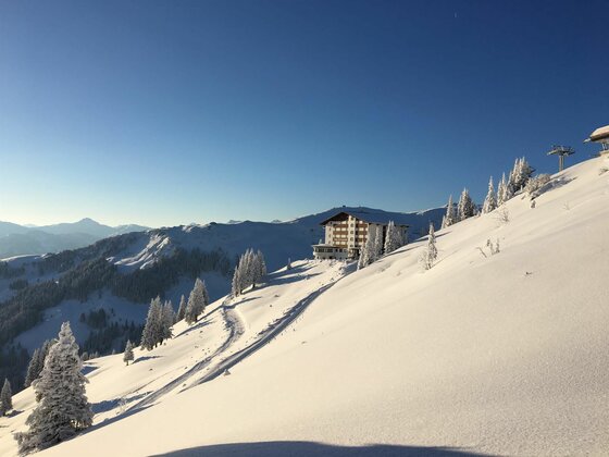 Ehrenbachhöhe im Winter Verschneiter Berghang mit einem großen Hotelgebäude unter blauem Himmel.