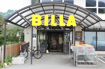 Billa Hammerschmiedstraße Eingangsbereich eines Billa Supermarktes mit gelbem Schriftzug, Glasvordach, Einkaufswagen und einem Fahrradständer.