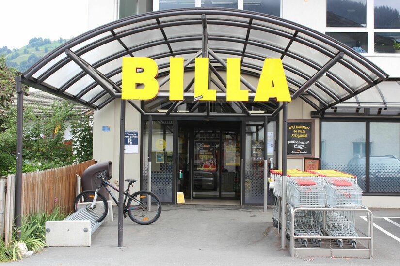 Billa Hammerschmiedstraße Eingangsbereich eines Billa Supermarktes mit gelbem Schriftzug, Glasvordach, Einkaufswagen und einem Fahrradständer.