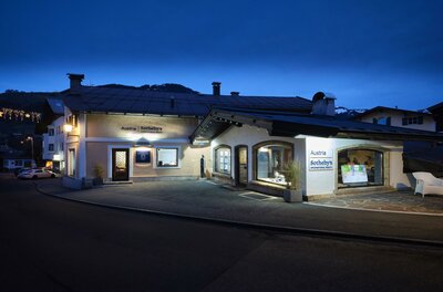 Ein charmantes Gebäude bei Nacht mit warm beleuchteten Fenstern. Die Straße ist ruhig und der Himmel ist dunkelblau.