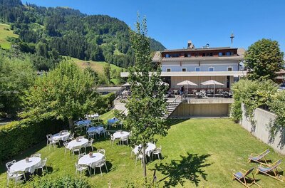 Außenansicht Gasthof Auwirt Außenbereich des Gasthof Auwirt mit gedeckten Tischen auf einer Wiese vor dem Gebäude und bewaldeten Bergen.