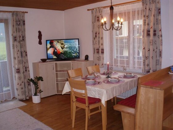 Essbereich mit gedecktem Holztisch, Stühlen, Eckbank und einem Fernseher im Hintergrund.