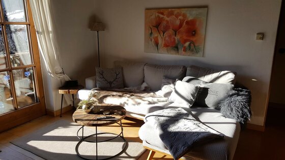 Helles Wohnzimmer mit grauem Ecksofa, rundem Holztisch und Blumenbild an der Wand.