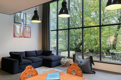 Moderner Wohnraum mit dunklem Sofa, Holztisch und großer Fensterfront zum Garten.