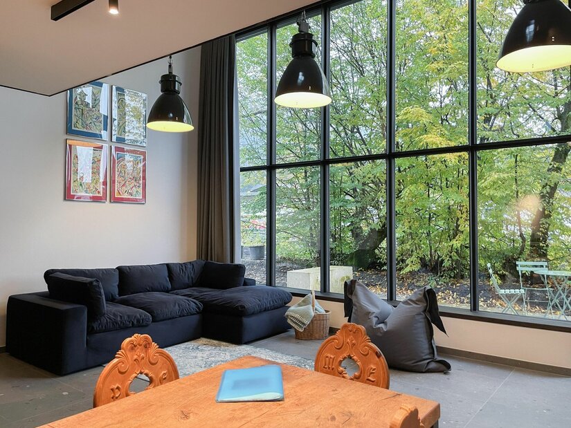 Moderner Wohnraum mit dunklem Sofa, Holztisch und großer Fensterfront zum Garten.