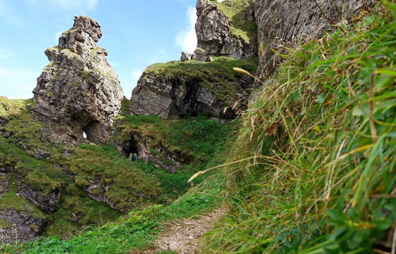 Schmaler Wanderpfad führt an markanten Felsformationen und grünen Grashängen vorbei.