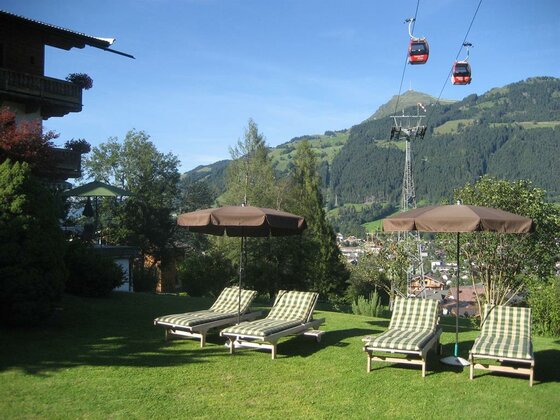 Garten mit Sonnenliegen und Sonnenschirmen vor einer Bergkulisse mit Seilbahn.