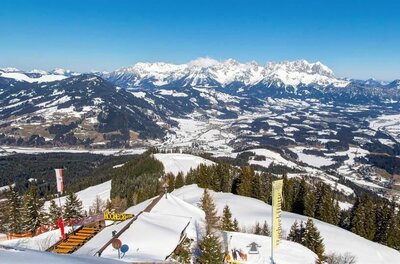 Blick von der verschneiten Hocheckhütte auf ein weites Tal und schneebedeckte Berggipfel unter blauem Himmel.