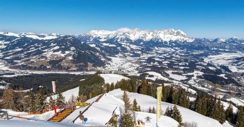 Winterpanorama von der Hocheckhütte Blick von der verschneiten Hocheckhütte auf ein weites Tal und schneebedeckte Berggipfel unter blauem Himmel.