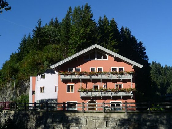 Gasthof Möllinger im Sommer Mehrstöckiges Gasthaus mit rötlicher Fassade, Holzbalkonen und Blumenschmuck vor bewaldetem Hang.