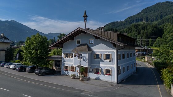 Ein charmantes Gebäude im alpinen Stil mit blauen Wänden und Fensterläden. Umgeben von Bergen und grüner Natur, bietet es eine einladende Atmosphäre.