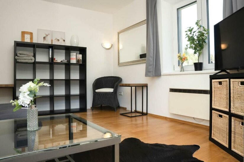 587402277 Ein modernes Wohnzimmer mit einem gläsernen Tisch, einem schwarzen Regal und einem Sofa. Große Fenster lassen viel Licht herein und sorgen für eine einladende Atmosphäre.