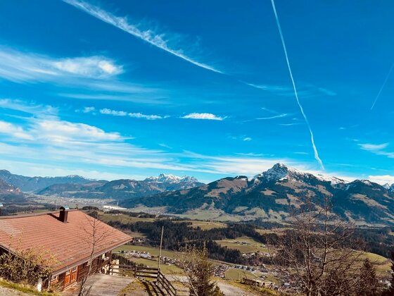Aussicht vom Hollenauer Kreuz Blick von einer Almhütte auf ein weites Tal und schneebedeckte Berggipfel unter blauem Himmel.