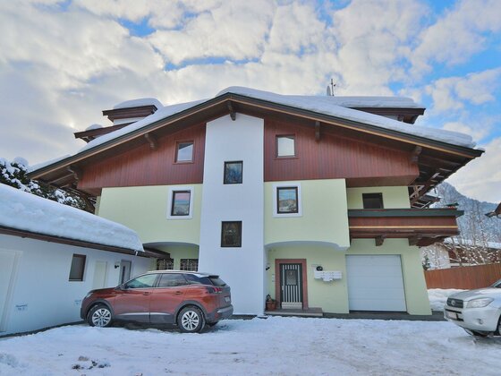Ein modernes Haus im Schnee, umgeben von einer malerischen Winterlandschaft. Der Himmel ist teilweise bewölkt und die Atmosphäre wirkt ruhig und einladend.