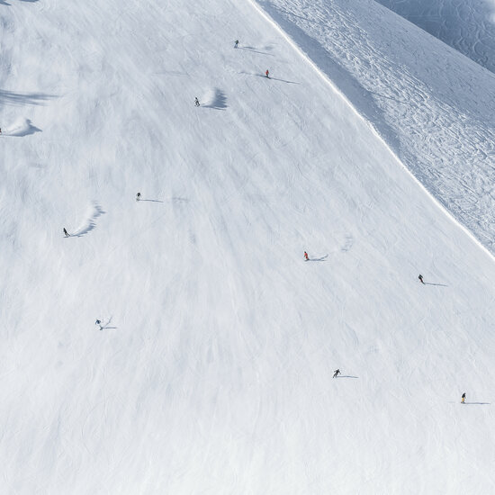 Eine weite, schneebedeckte Skipiste in Kitzbühel, auf der mehrere Skifahrer in verschiedenen Farben unterwegs sind.