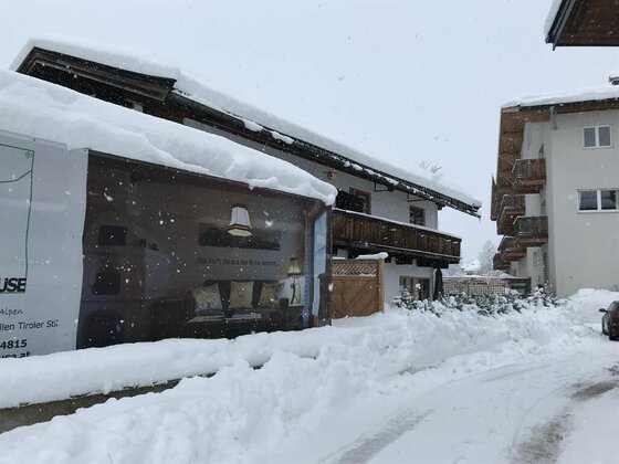 Winteransicht Kitzalphouse Apartments Verschneite Gebäude mit hohen Schneelasten auf den Dächern und einer geräumten Straße im Vordergrund.