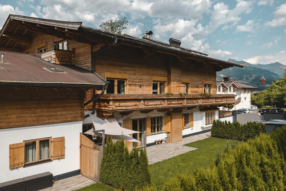 Hausansicht seitlich Zweistöckiges Holzhaus in alpiner Bauweise mit Balkon, Garten und Blick auf eine Seilbahngondel.