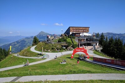 Berghaus auf einem Gipfel mit befestigten Wanderwegen und einem roten Torbogen unter blauem Himmel.