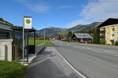 Bushaltestelle an einer Landstraße mit Bergen im Hintergrund.