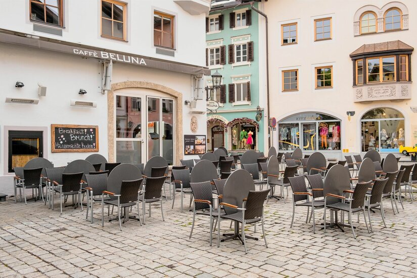 Café Beluna Außenansicht Außenbereich eines Cafés mit Tischen und Stühlen auf einem gepflasterten Platz vor historischen Gebäuden.