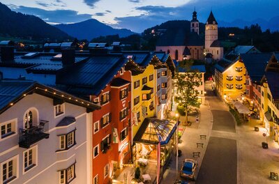 Vorderstadt Abendstimmung Beleuchtete Häuserzeile in einer gepflasterten Altstadt bei Dämmerung mit Bergen im Hintergrund.