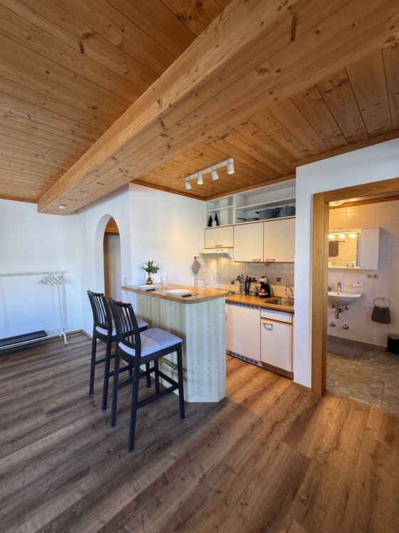 Blick von oben auf eine Küchenzeile mit Holztresen, zwei Barstühlen und angrenzendem Badezimmer.