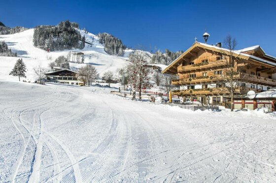 Präparierte Skipiste vor einem traditionellen Holzhotel in den Alpen bei sonnigem Wetter.