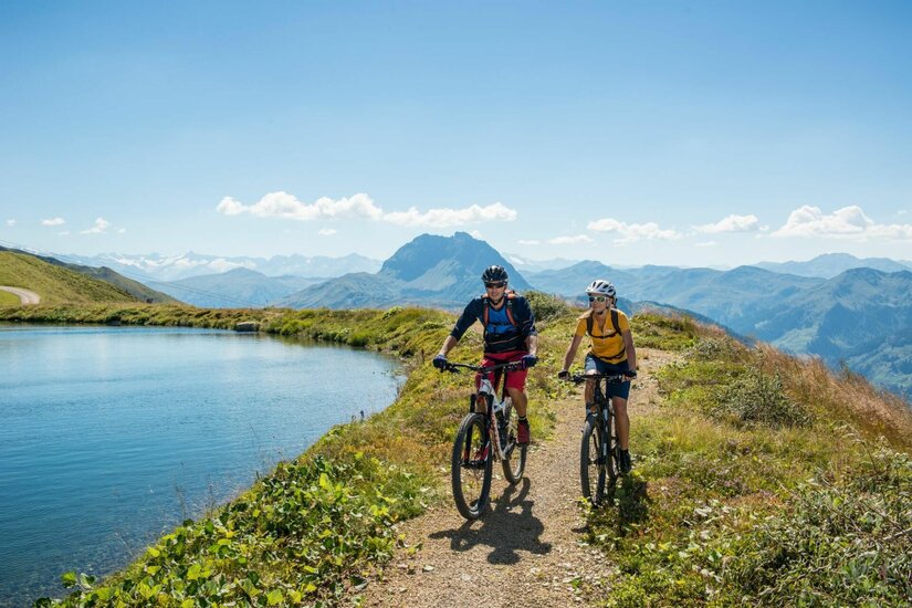 Mountainbiken am Bergsee Zwei Mountainbiker fahren auf einem Schotterweg an einem Bergsee vorbei.