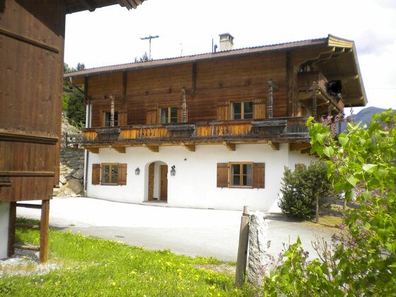 Haus Gletscherblick Zweistöckiges alpines Wohnhaus mit weißem Erdgeschoss, Holzobergeschoss und umlaufendem Balkon.