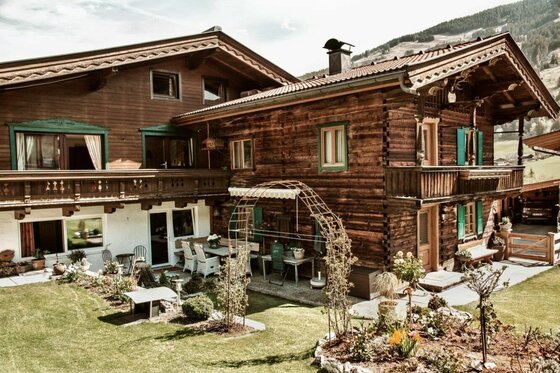 Jagahäusl Jochberg im Sommer Zweistöckiges Holzhaus im alpinen Stil mit Garten, Terrasse und Balkon vor bewaldetem Hang.