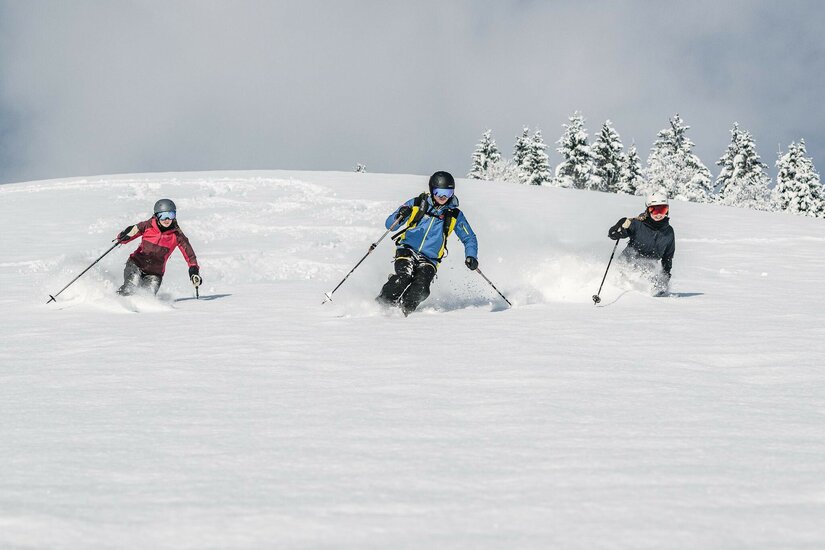 Skifahrer im Tiefschnee Drei Skifahrer fahren nebeneinander durch tiefen Pulverschnee auf einem Hang.