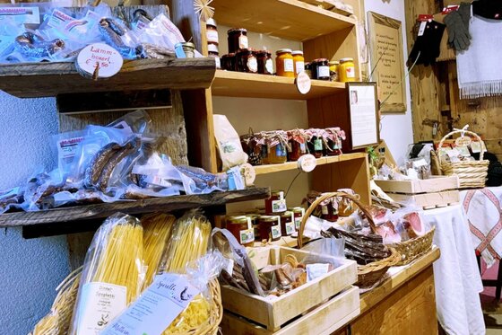 Hofladen 1709 Ein Regal mit verschiedenen regionalen Lebensmitteln, darunter Pasta, Marmelade und Snacks. Die Ware ist liebevoll präsentiert und verstärkt den rustikalen Charme des Geschäfts.