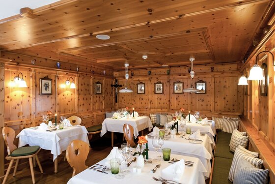 Zirbenstube im Hotel Kaiserhof Rustikale Gaststube mit Holzvertäfelung an Wänden und Decke sowie eingedeckten Tischen.