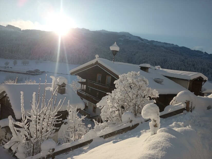Hennleiten Winter 24 Verschneite Holzhäuser in einer alpinen Winterlandschaft bei tiefstehender Sonne.
