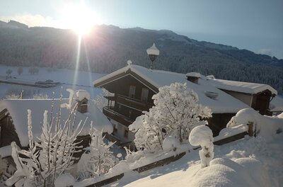 Hennleiten Winter 24 Verschneite Holzhäuser in einer alpinen Winterlandschaft bei tiefstehender Sonne.