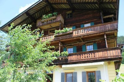 Grünberghof Ein traditionelles Holzhaus mit mehreren Balkonen und grünen Pflanzen. Der Himmel ist klar und sonnig.
